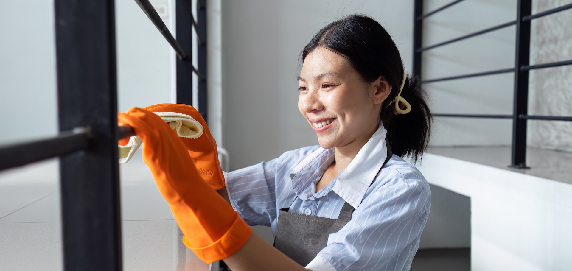 Hands in blue rubber gloves holding microfiber cleaning cloth make cleaning and disinfection for good hygiene of a stair railing.